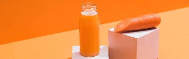 fresh juice in glass bottle near ripe carrot on cubes on orange background, panoramic shot - Foto, afbeelding