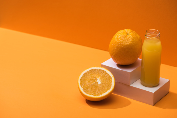 zumo fresco en botella de vidrio cerca de naranjas y cubos blancos sobre fondo naranja
 - Foto, Imagen
