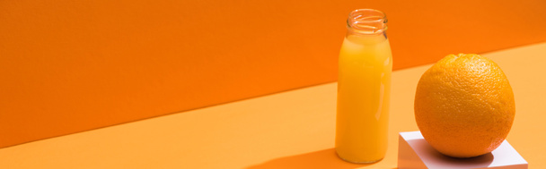 frischer Saft in Glasflasche in der Nähe von Orangen- und Weißwürfel auf orangefarbenem Hintergrund, Panoramaaufnahme - Foto, Bild
