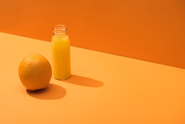 fresh juice in glass bottle near whole orange on orange background - 写真・画像