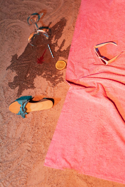 Gevallen cocktailglas en vintage damesschoen naast roze handdoek - Foto, afbeelding