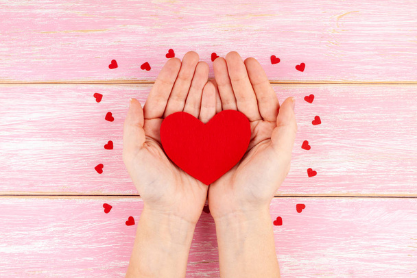 Kobieta Ręce trzymając czerwone serce na różowym drewnianym tle z Red Confetti Hearts - Zdjęcie, obraz