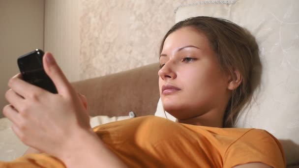 Fiatal nő arca. A boldog nő portréja jó szórakozást az ágyban. mobiltelefont használ - Felvétel, videó