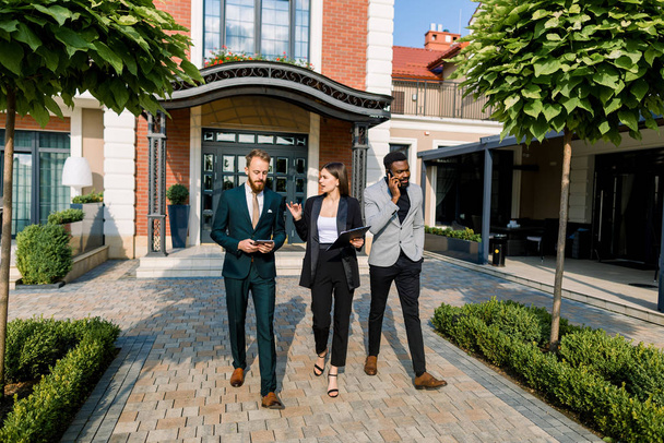 Full length of young three smiling multiracial businesspeople discussing about a meeting while walking outdoors in front of modern building, office or restaurant or hotel - Foto, afbeelding