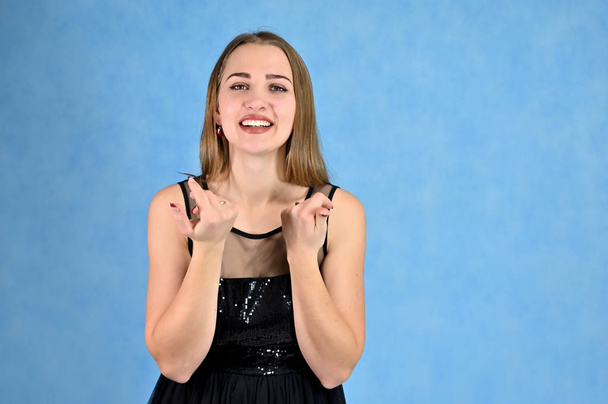 Universal concept horizontal portrait of a woman on a blue background. A photo of a pretty smiling girl with long hair and excellent make-up in a black dress stands in different poses. - Zdjęcie, obraz