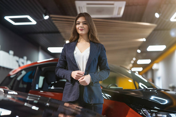 beautiful brunette woman manager in business suit standing in electric car dealership center - Foto, Imagen