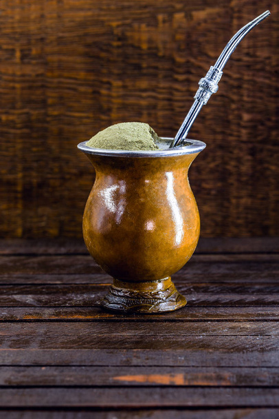 Chimarrão, or mate herb, is a South American drink left by indigenous cultures. It consists of a gourd, a pump, ground yerba mate and boiling water. Chimarrão isolated on wooden background. Copy space - Photo, image
