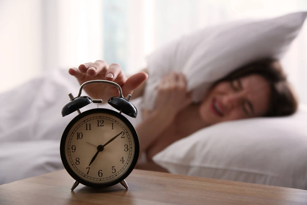 Young woman turning off alarm clock at home in morning, focus on hand - Valokuva, kuva