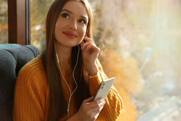 Woman listening to audiobook near window in cafe - 写真・画像