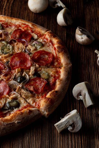 Закрыть горячую и пряную пиццу с халапеньо, пепперони и красным луком на темном деревянном фоне
 - Фото, изображение