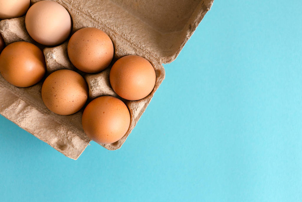 Fresh brown and speckled chicken eggs in eco cardboard on a blue background. Photo with soft focus, macro shot. - 写真・画像