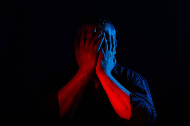 Closeup portrait of man in neon light. Human emotions, facial expression, headache, hands on face. Concept of human emotions - Photo, Image