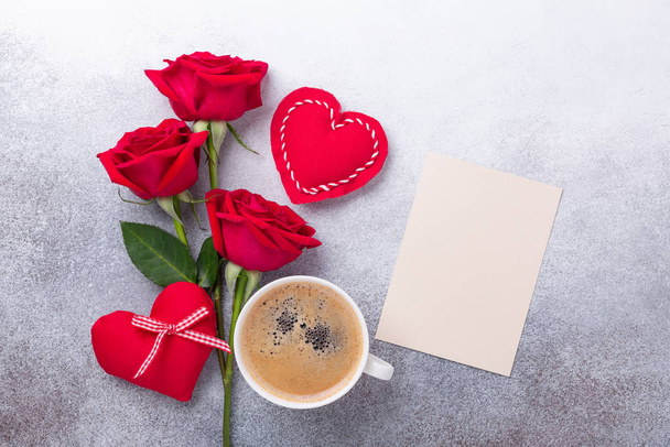 Valentines day greeting card. Coffee cup, red roses and textile heart on stone background. Top view - 写真・画像