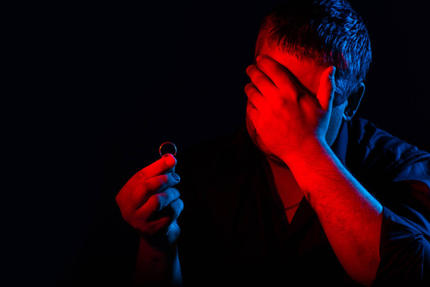 Closeup portrait of man in neon light. Human emotions, facial expression, headache, reflections on the past, wedding ring in hand - Foto, afbeelding