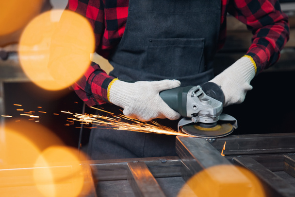 Werkman hand met elektrisch wiel slijpen op staalconstructie in fabriek, lichte vonk - Foto, afbeelding