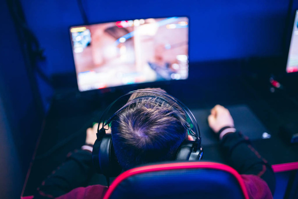 Profesionální hráč hraní online her turnaje PC počítač se sluchátky, rozmazané červené a modré pozadí - Fotografie, Obrázek