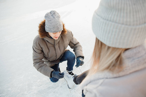 Чоловік допомагає одягати білі фігурні ковзани для ковзанки красивій молодій дівчині на тлі снігу взимку, концепція піклування про любов, відносини між людьми
 - Фото, зображення