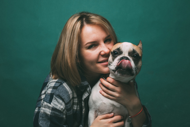 jong meisje en knuffelt een franse bulldog op een groene achtergrond - Foto, afbeelding