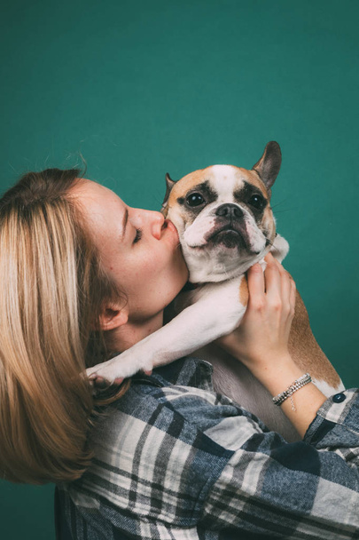 young girl and hugs a french bulldog on a green background - Zdjęcie, obraz