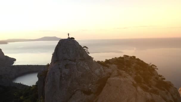 Schießen von oben auf die Person, die den Berg Karaul-oba auf der Krim, Ukraine erobert hat. der berühmte Berg der Halbinsel am Abend vor dem Hintergrund des Sonnenuntergangs und des Schwarzen Meeres. Mann an der Spitze. - Filmmaterial, Video