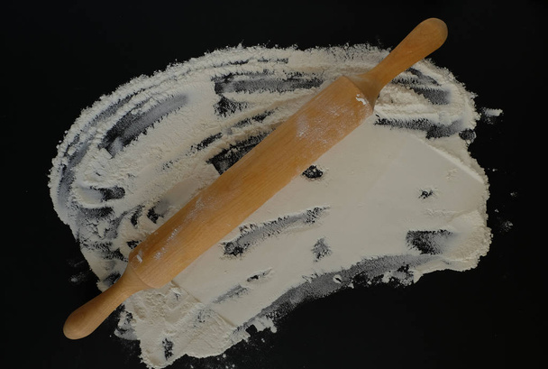 A little flour and a rolling pin to roll out the dough on a black flat surface. View from above. - Photo, Image
