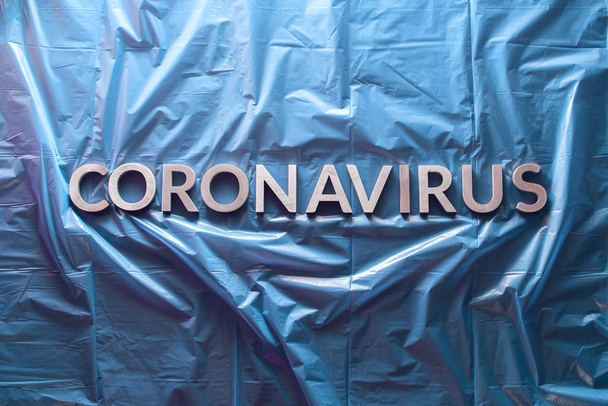 słowo koronawirus ułożone srebrnymi literami na pogniecionej niebieskiej folii z tworzywa sztucznego - płaska leżała w środku kompozycji - Zdjęcie, obraz