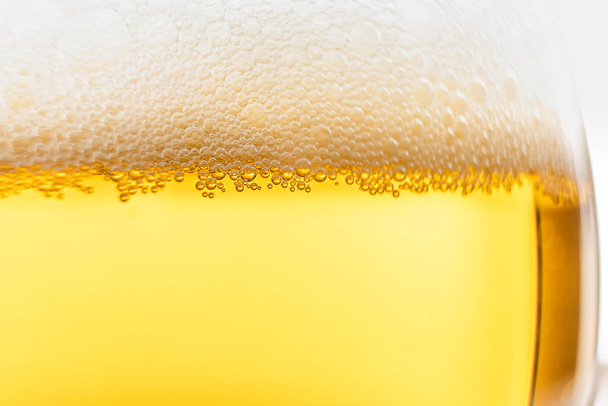 Ελαφριά μπύρα σε ποτήρι, μακροφωτογραφία. Πάνω είναι αφρός. Αφηρημένη εικόνα φόντου ενός ποτού. - Φωτογραφία, εικόνα