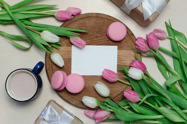 Taza de café, flores de tulipán de primavera y macarrones rosados en la vista superior de la mesa pastel. Saludo para el Día de las Mujeres o Madres
 - Foto, imagen
