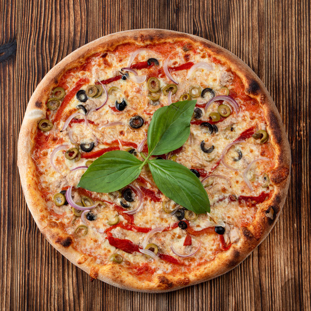 Вид сверху круглой пиццы с красным луком, черными и зелеными оливками, плавленым сыром и кетчупом на ржавом текстурированном фоне
 - Фото, изображение