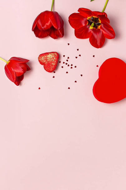 赤いチューリップ、赤いハート型のギフトボックス、パステルピンクの背景トップビューの紙吹雪フラットレイコピースペース。母の日、バレンタインデー、誕生日、休日の背景。春の花、素敵なグリーティングカード - 写真・画像