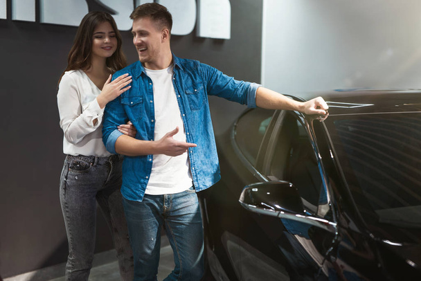 young happy couple handsome man and beautiful woman checking new car interior while standing in electric car dealership center - Φωτογραφία, εικόνα