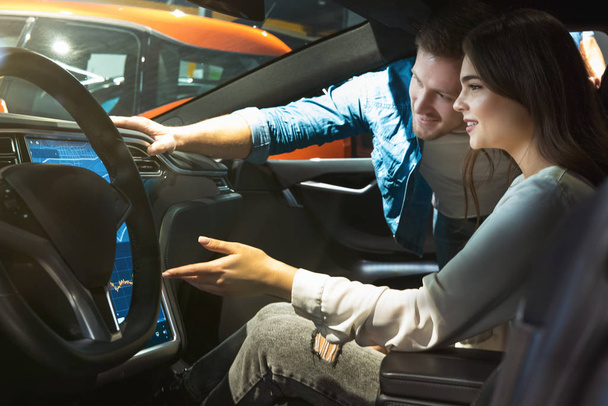 young couple man and woman checking modern gps navigation system in new vehicle during electric car dealership center visit - 写真・画像