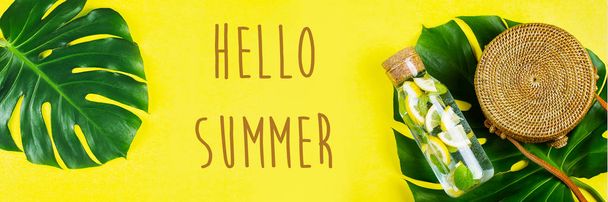 Hola Summer Banner para el sitio web. Bolsa de ratán redonda y botella de vidrio con limonada y hoja de Monstera. Fondo amarillo, soleado. Piso tendido, vista superior
 - Foto, Imagen