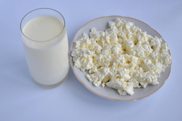 Cottage kaas op een bord en een glas melk. - Foto, afbeelding