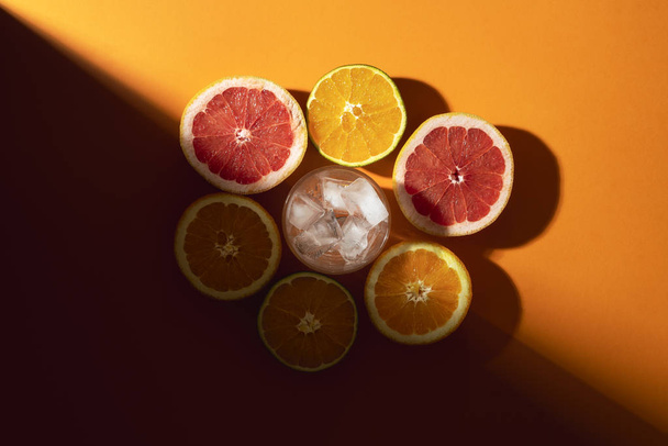 Citrus fruits and glass with ice in sunlight. Making cold drink - Fotoğraf, Görsel