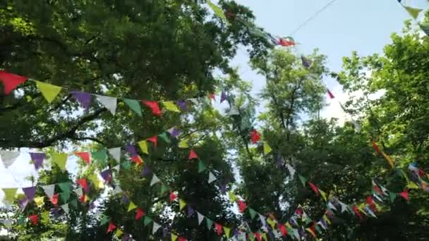 Bayram için renkli kağıt bayraklardan oluşan bir çelenk. Çocukların doğum günü partisi için bir sahne. Doğayı ağaçların arka planına karşı süslemek. Bunting flaması - Çarşaflardan renkli bayraklar. - Video, Çekim