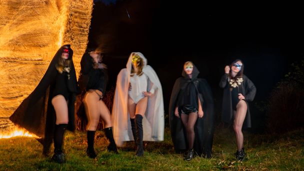 mystery young girls wearing black and white cloaks, witch's sabbath in the woods at the night by the bonfire - Photo, image