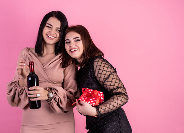 Duas mulheres sensuais rindo segurando uma garrafa de vinho e uma caixa de presente no fundo rosa
 - Foto, Imagem