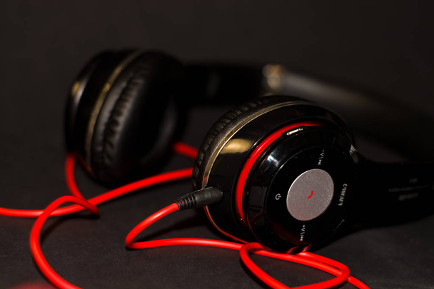 Op zwarte achtergrond, grote hoofdtelefoon voor het luisteren naar muziek met rode elementen en koord.  - Foto, afbeelding