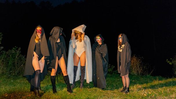 mystery young girls wearing black and white cloaks, witch's sabbath in the woods at the night by the bonfire - Photo, Image