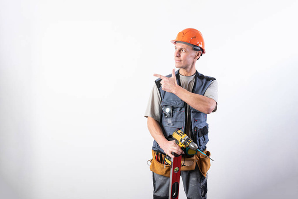 O construtor aponta para a esquerda. Oferece com dedos indicadores. Em roupas de trabalho e chapéu duro
. - Foto, Imagem