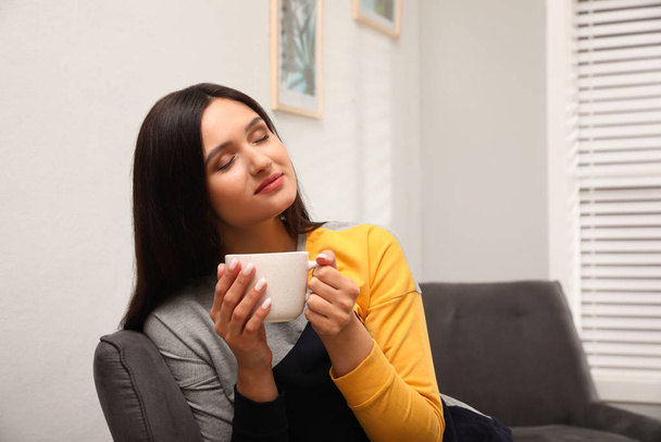 Giovane donna con tazza di bevanda rilassante a casa
 - Foto, immagini