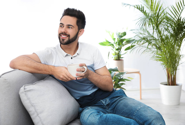 Young man with cup of drink relaxing on couch at home - Foto, Bild