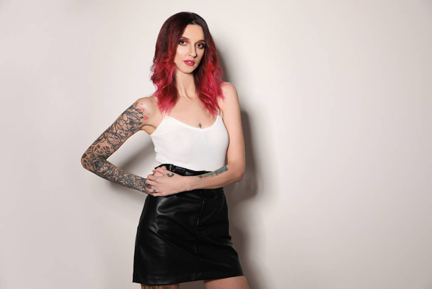 Beautiful woman with tattoos on arms against light background - Foto, afbeelding