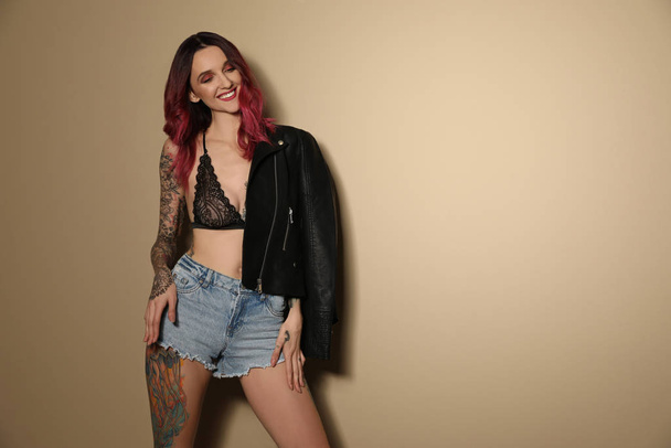 Beautiful woman with tattoos on body against beige background. Space for text - Foto, immagini