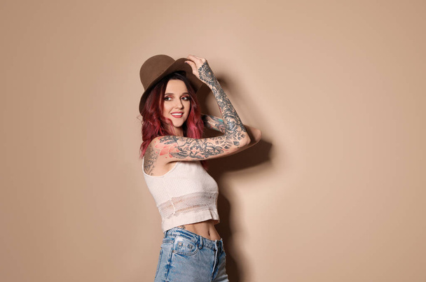 Beautiful woman with tattoos on body against beige background - Zdjęcie, obraz
