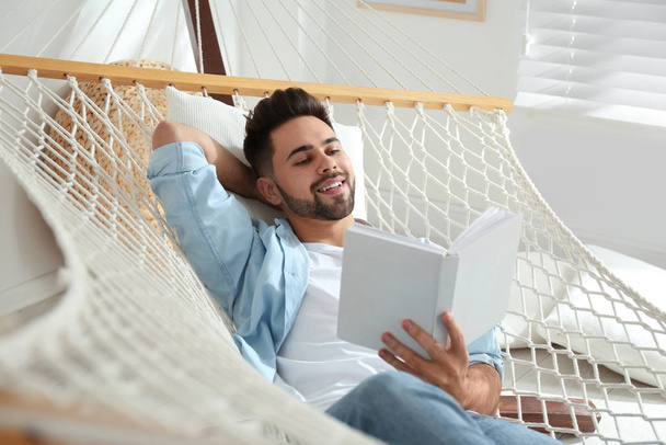 Young man reading book in hammock at home - Foto, imagen