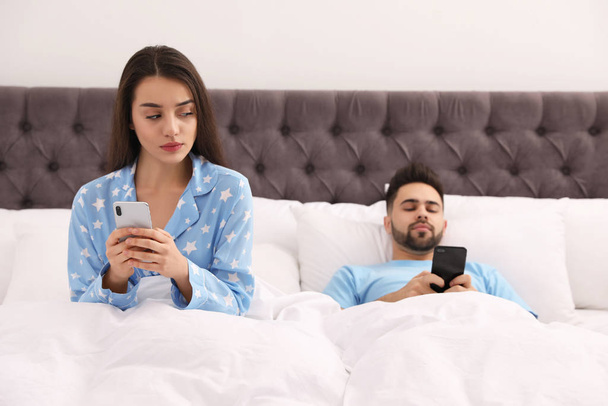Young couple with smartphones in bed at home - Fotoğraf, Görsel