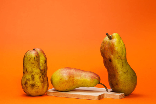 Two ugly pears and one beautiful on an orange background. - Фото, изображение