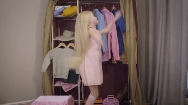Blond Caucasian little girl in pink dress jumping and spinning in front of wardrobe at home. Cheerful beautiful child having fun on weekends indoors. Joy, lifestyle, childhood. - Video, Çekim